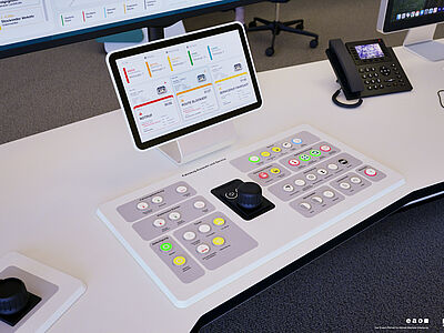 Eine Konsole mit Knöpfen und ein Monitor auf einem Schreibtisch.